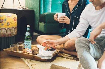 a man and a woman sitting on the floor with a tray of food and drinks at Villa Carlotta – Furnished Apartments, Los Angeles, 90028